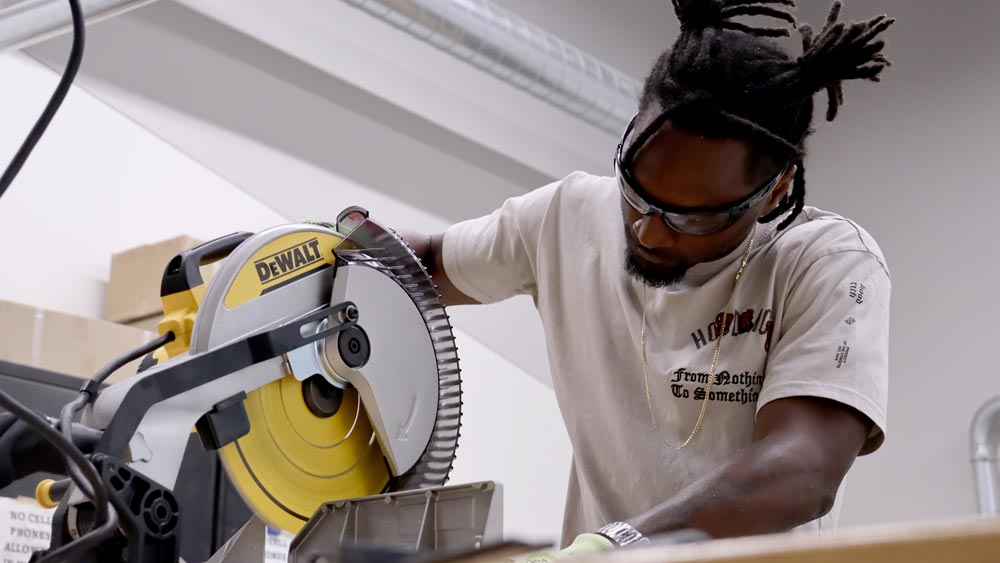 KCC CEJA student cutting materials with a miter saw.